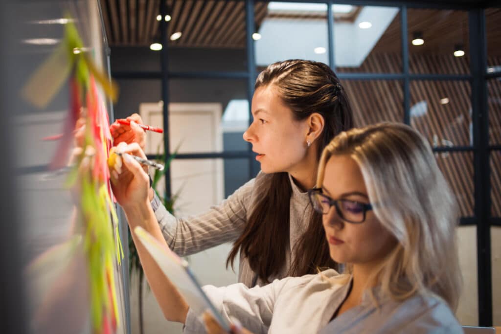 Two people writing on a board practicing the collaborative principle of Agile.