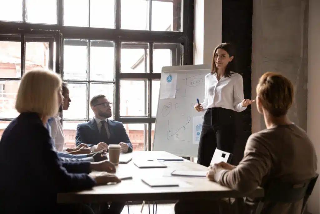 Leader standing in front of a whiteboard speaking to her team.