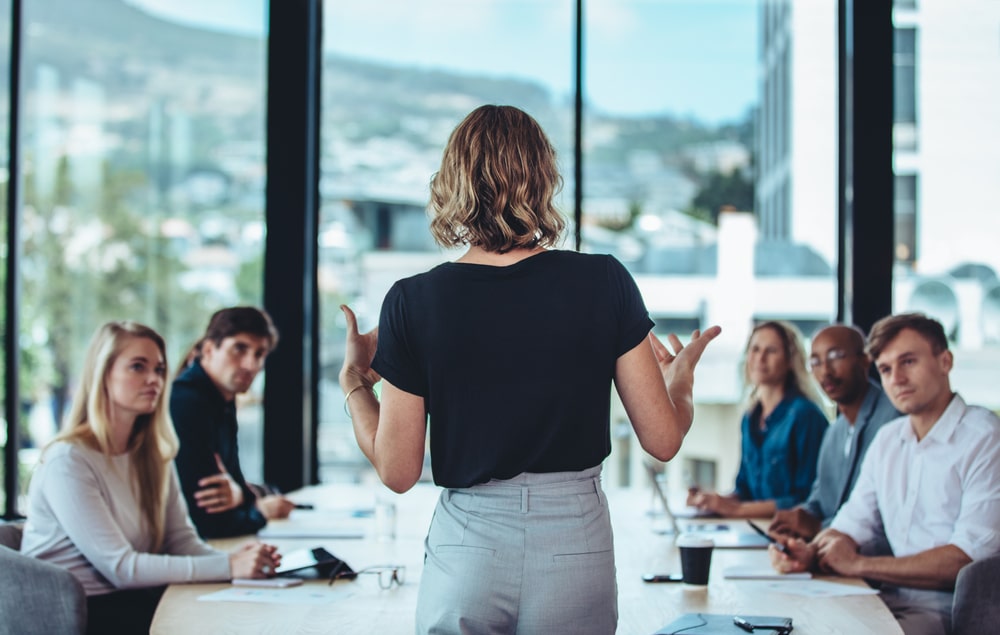 Leader standing at the end of the table speaking to colleagues.